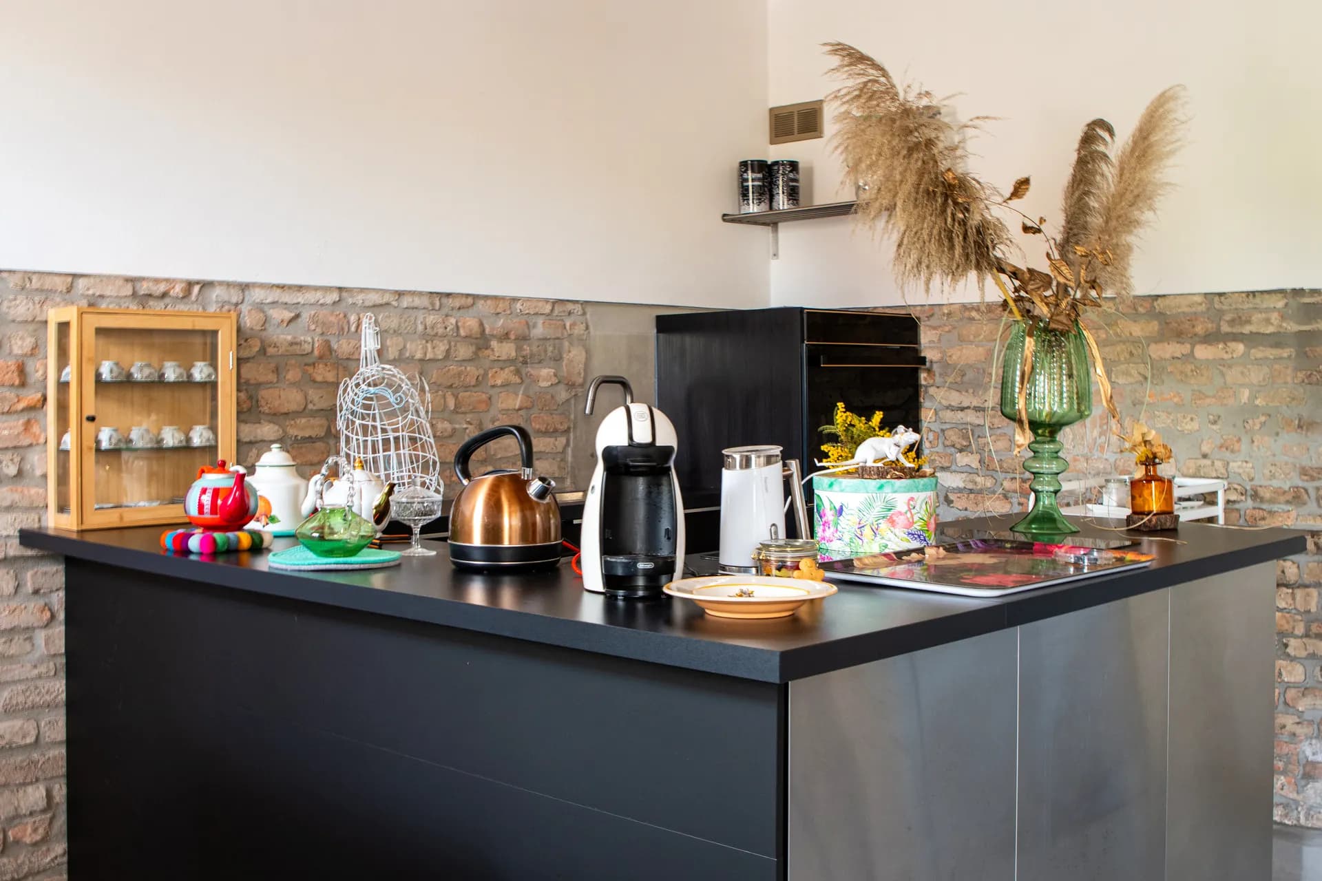 Angolo cucina con bollitore in rame, macchina del caffè e muro a mattoni a vista